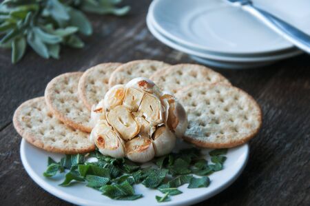 Appetizer of roasted garlic with crackers and herbsの写真素材