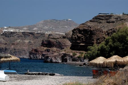black sand beach under cliff caldera with taverna greek islandsの写真素材