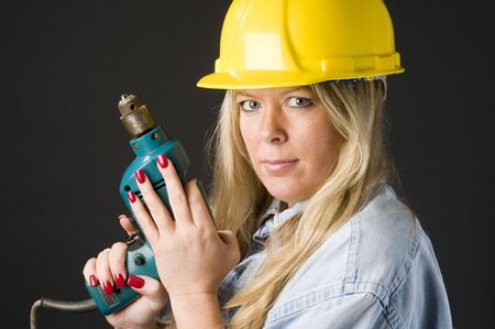 pretty home repair woman and contractor with drill and yellow protective hard hatの写真素材