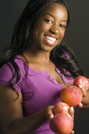 pretty latina hispanic african american woman smiling and offering variety of plums pluots and healthy fresh fruitの写真素材