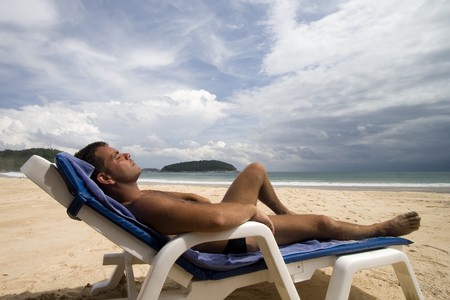 tanned man laid on a chair at a white sand beach, Phuket Island, Thailandの写真素材