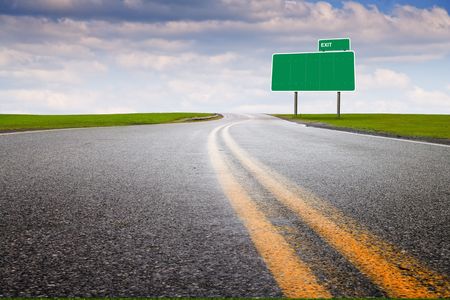 Asphalt pavement through green grass meadow with blank signの写真素材