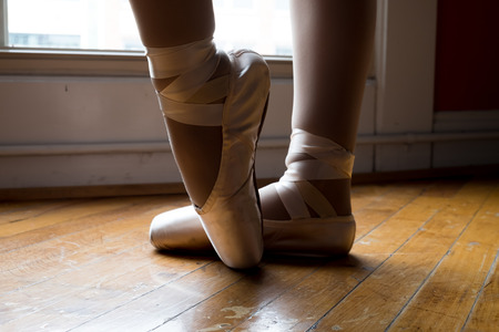 Ballerina wearing pointe shoes near window, knee down wooden floor
