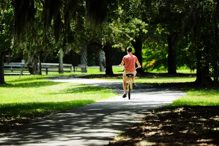 Picture from behind of your male riding a bike on a paved path through the trees and moss of SC.