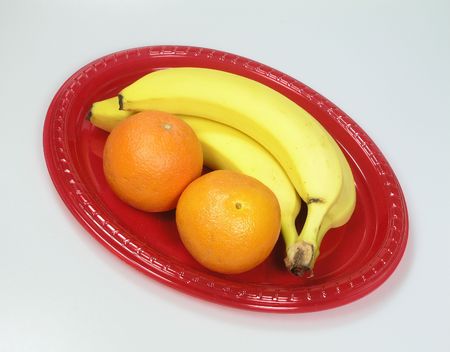 Banana and orange still life on a red platter with gray backgroundの写真素材