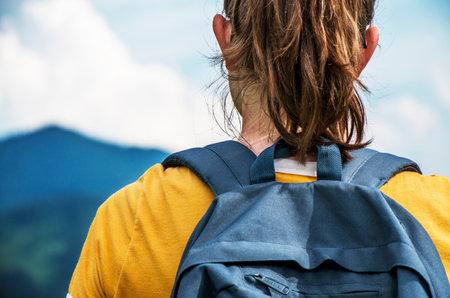 Close up of a girl with backpack on a trip in mountains with blue hills and sky in the background
