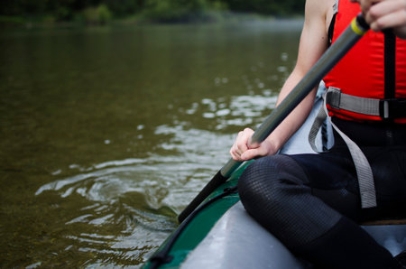 Close up of a man wearing a safety vest and holding a paddle on a boat - summer sport activities