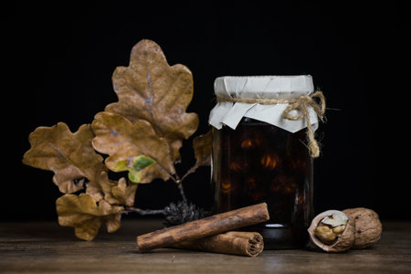 Autumn atmospheric vintage still life with jar full of nuts, walnuts, cinnamon and dried leaves on wooden board with dark backgroundの写真素材