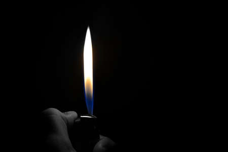 A hand lighting up a lighter with flame and dark backgroundの写真素材