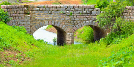 Old stone single arch bridge, Latvia. Famous ancient stone arch single track road bridge in the forest. View of small river and trees reflection in the water.の写真素材