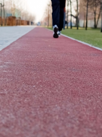 A person is jogging in blue tracksuits and trainers on a red, rubber covered running track