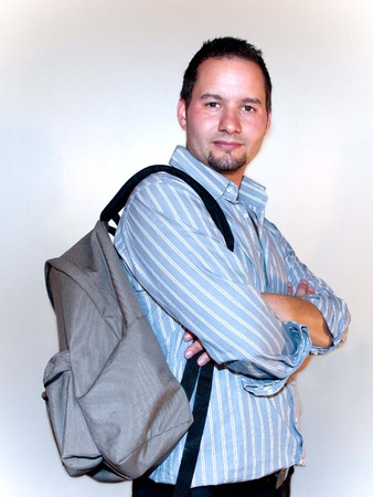 A man is standing with a brown backpack with folded arms in gray shirt
