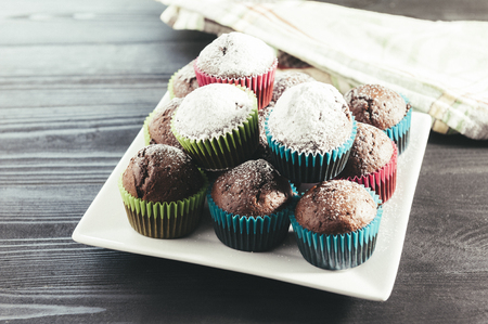 Chocolate muffins sprinkled with icing sugar on a white plateの写真素材