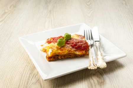 an appetizing portion of lasagna on a white plate topped with tomato sauceの写真素材