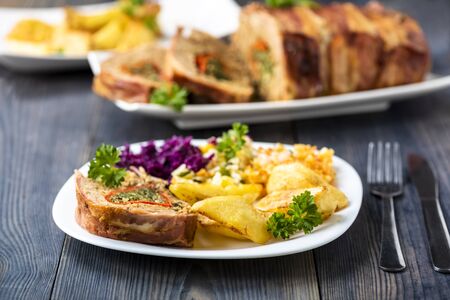 a piece of minced meat roulade stuffed with spinach, served with baked potatoes and a set of saladsの写真素材