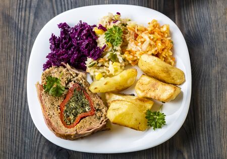 a piece of minced meat roulade stuffed with spinach, served with baked potatoes and a set of saladsの写真素材