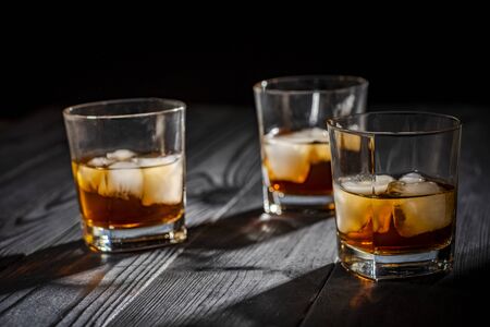 a glass of whiskey with ice on a wooden black tableの写真素材
