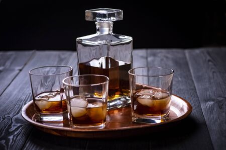 A tray with a carafe and three glasses of whiskey on a wooden black tableの写真素材