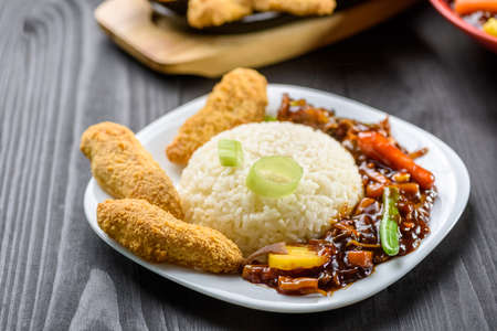 rice with vegetables in sweet and sour sauce and chicken tenderloin on white plateの写真素材