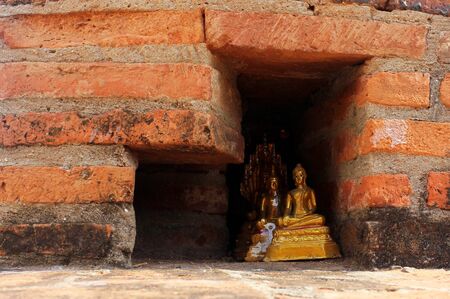 Small golden buddha statues hidden in a red brick wall.の写真素材