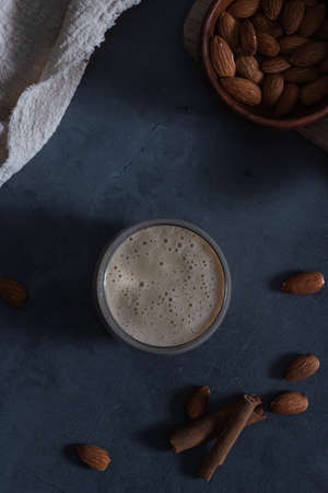 Tasty smoothie with banana and almond milk in a glass. On a dark gray concrete stone background,...