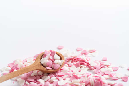 Spoon full of sweet decorative pink and white hearts. Baking decorations, Sugar hearts in a wooden measuring spoon, close up. Space text. Horizontal.の写真素材