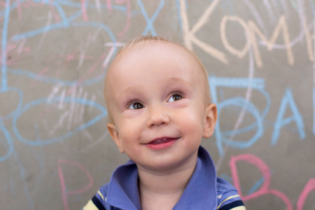 joyful little boy looks forward up sitting at a concrete wall