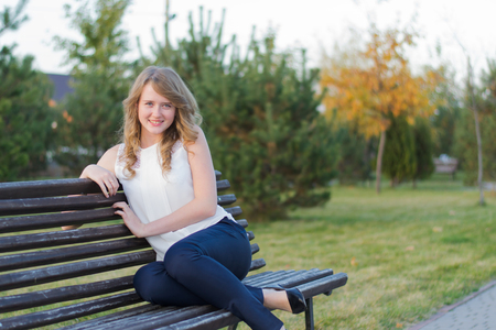 funny, beautiful girl sitting on a bench in autumn parkの写真素材
