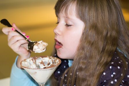 little girl with pleasure eats dessert in cafe close-upの写真素材