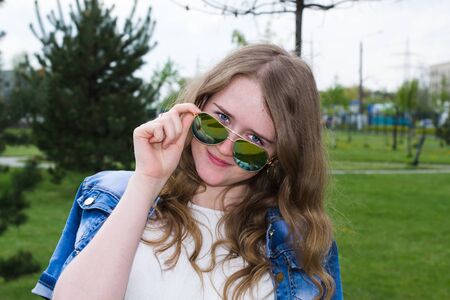 Young cheerful girl in sunglasses, close-up, outdoors, looking forward over her glassesの写真素材