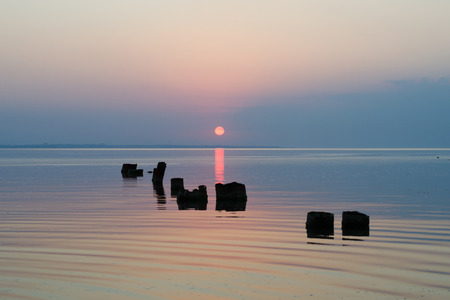 bright blue sunset with reflection in sea surface above the sea surface with piles sticking out of...