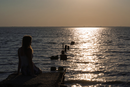 girl sitting on the pier and watching the sea at sunsetの写真素材