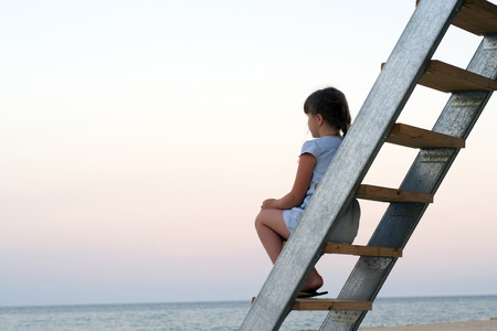 little girl sitting on a deserted beach looking at the seaの写真素材