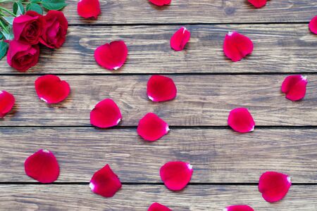 Three red roses and rose petals on the wooden background with a place for inscriptionの写真素材