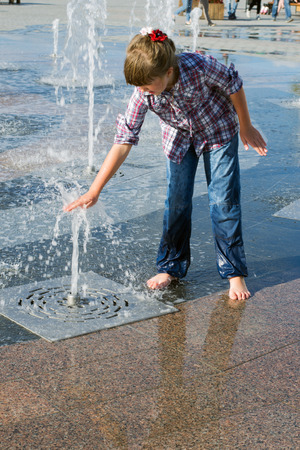 little girl 8 years in wet jeans and shirt playing in the fountain in the summer parkの写真素材