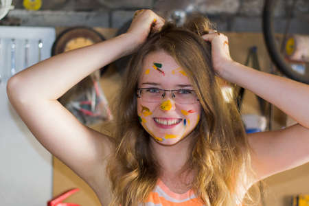 cheerful girl grimaces stained with paint on his face holding hands on the hair in the garageの写真素材