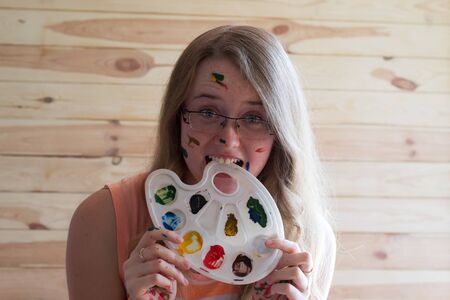 thoughtful girl with glasses in hand with paints and paint-stained faceの写真素材