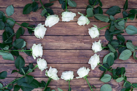 circle of white roses with green leaves on a background of brown wood planks, with a place for an inscriptionの写真素材