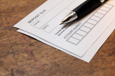 paper deposit slip and pen over wood background