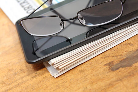 Newspaper with tablet and eye glasses on wood surface