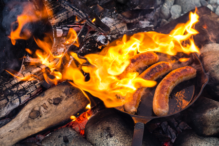 Live fire cooking juicy sausages over campfire.の写真素材