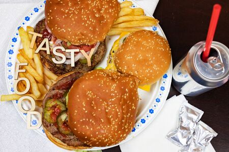 Juicy burgers and fries on a paper plate with words TASTY FOOD on burgers.の写真素材