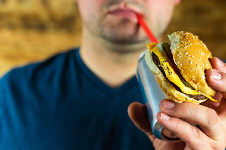 Man with burger and can of pop drink.