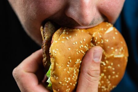 The hungry young man aggressively eats a burger. Fast food