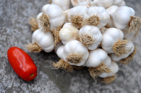 Garlic bulbs braid and one tomato on a gray raw stone tableの写真素材