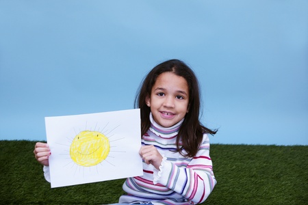 Young girl sitting in the grass holding a picture of the sunの写真素材