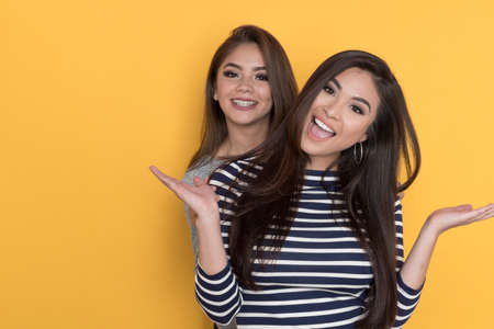 Two female teen friends on a yellow backgroundの写真素材