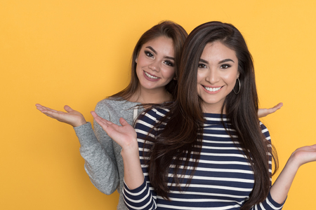 Two female teen friends on a yellow backgroundの写真素材
