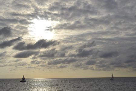 Picture of two sailboats under a partially covered  sun sailing the Pacificの写真素材
