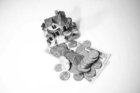 Pile of US dollars (coins and bills) with a miniature house on topの写真素材